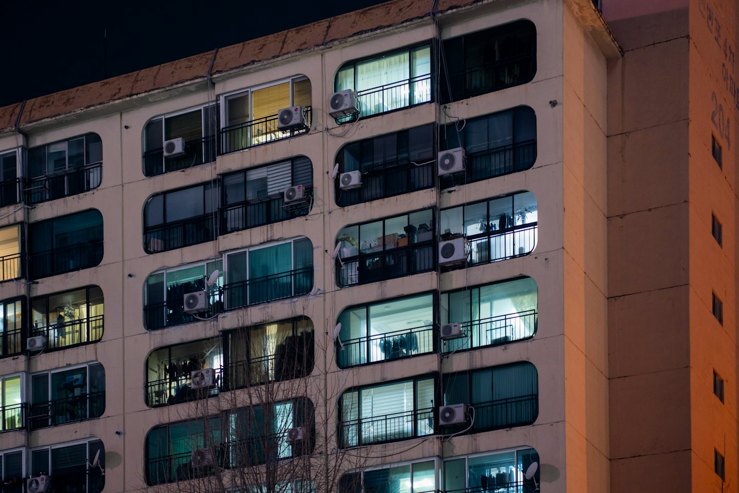 Apartment building at night with many lit windows and trees.