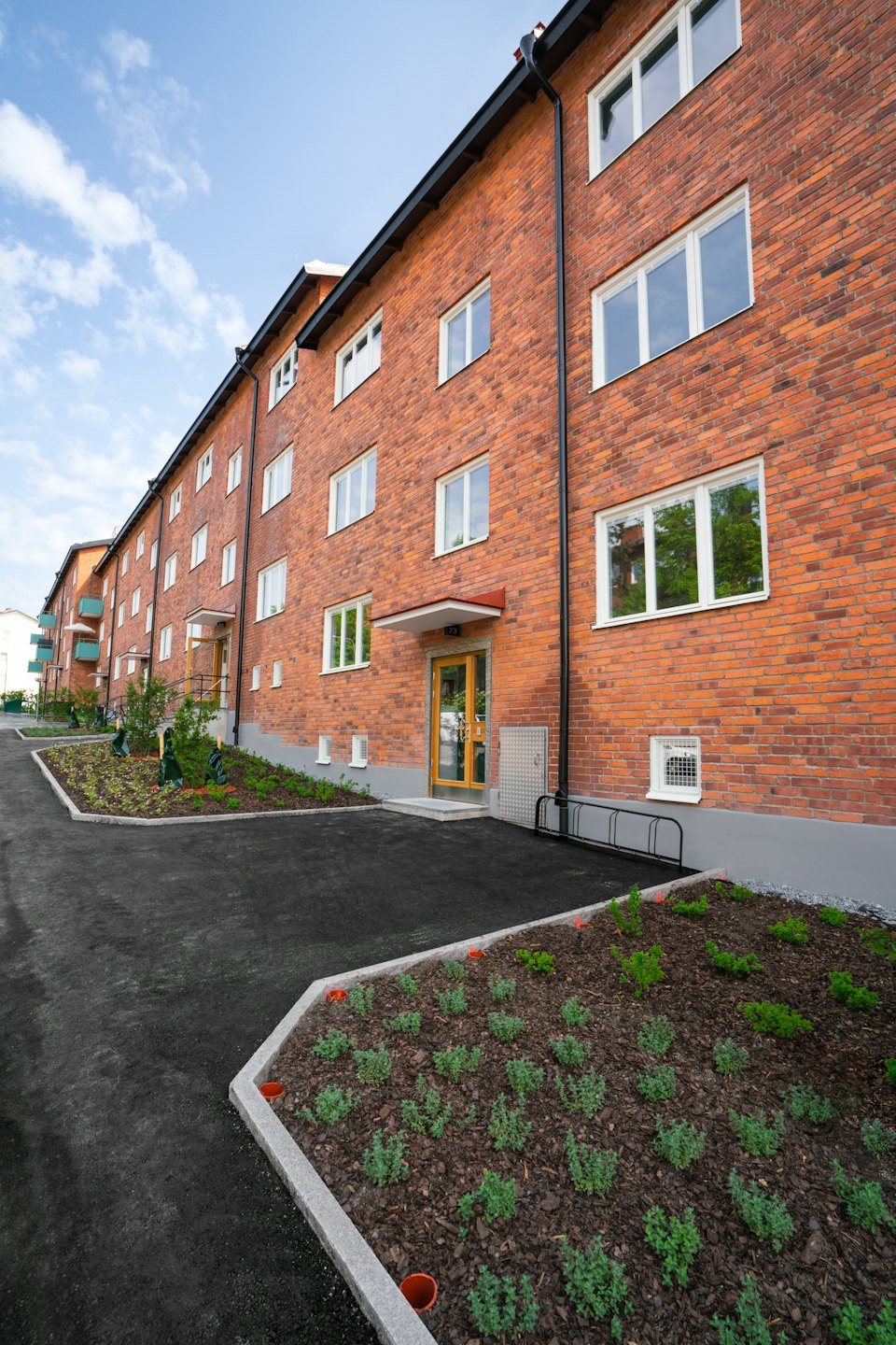 Multi-story brick apartment building with landscaped garden beds and paths.