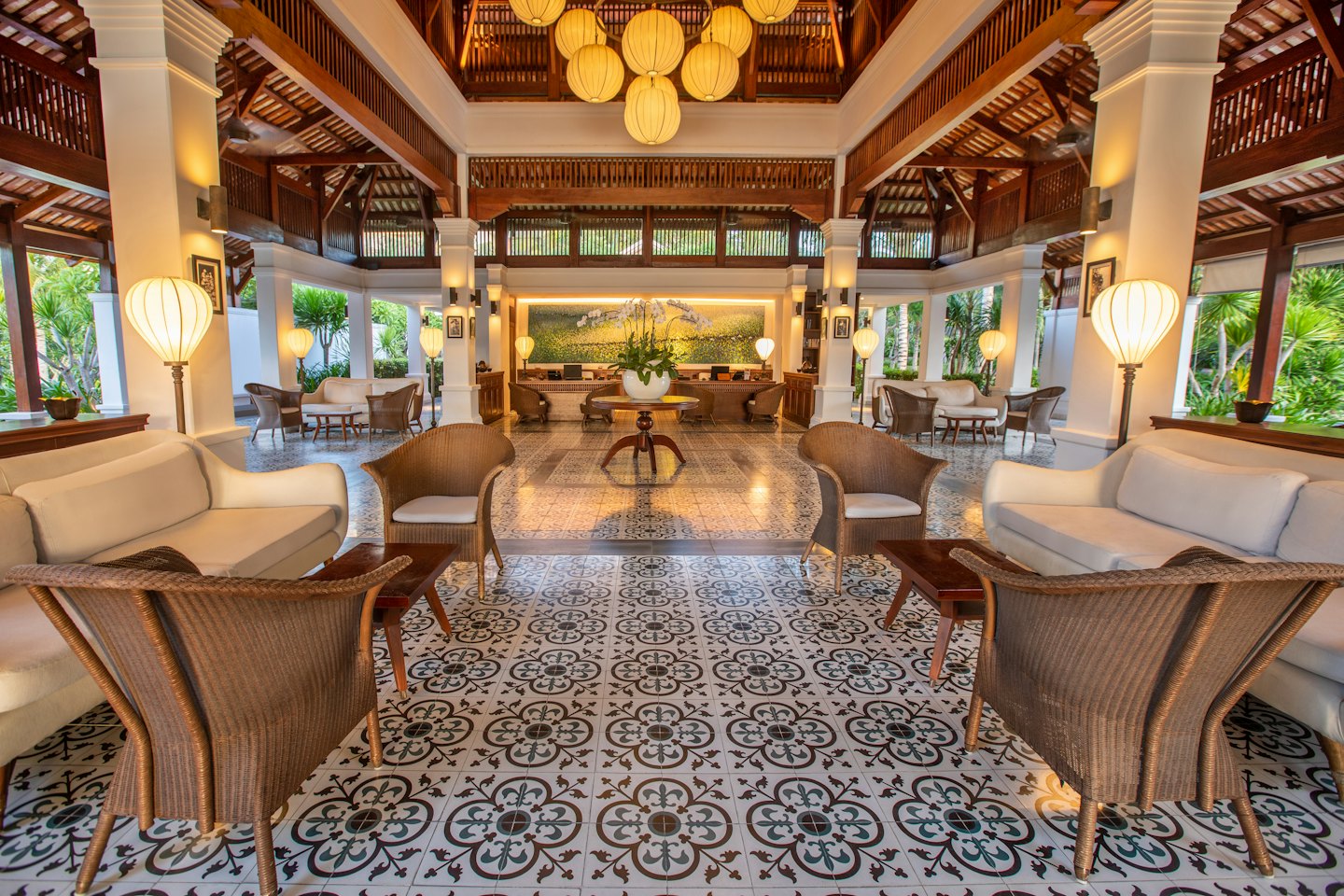 Hotel lobby with seating areas and lush greenery outside.